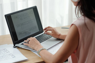 Woman reviewing website design on laptop amidst bright workspace, concentrating on layout and...