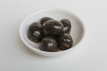 Table olives or fermented black olive, in small white bowl, isolated on white background
