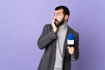 Adult reporter man with beard holding a microphone over isolated purple background is a little bit...