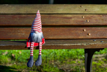 A Christmas gnome with a red and white striped knitted hat sitting on a wooden bench in the park on...