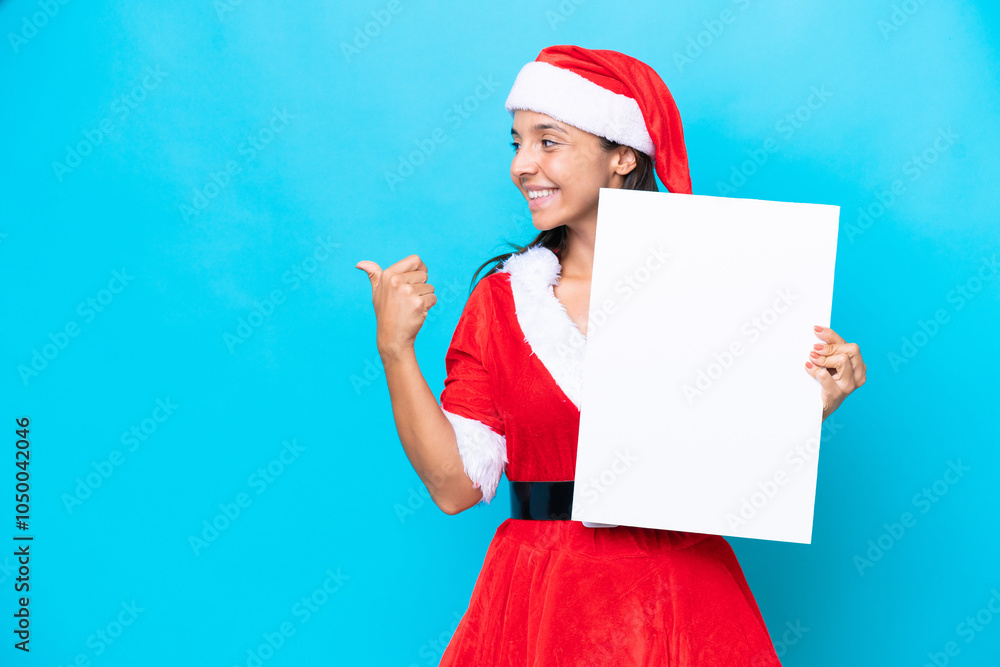 Wall mural young hispanic woman dressed as mama noel isolated on white background holding an empty placard and 