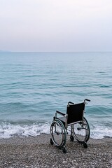 Fototapeta premium Wheelchair is sitting on the beach next to the ocean. The chair is black and green, and it is facing the water. The scene is peaceful and serene, with the ocean waves gently lapping at the shore