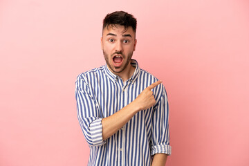 Young caucasian man isolated on pink background surprised and pointing side