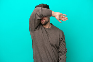 Young caucasian man isolated on blue background covering eyes by hands