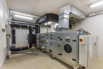 A large air handling unit is installed in a commercial utility room, featuring extensive ductwork...