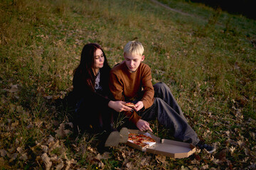 15-year-old teenage couple in love eating pizza on a picnic in an autumn park