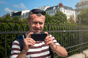 Fototapeta premium Male tourist taking photos on phone in the city. Young man takes a selfie with his smart phone.