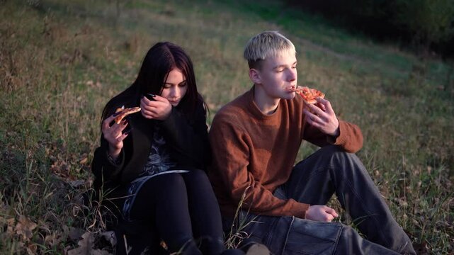       a 15-year-old teenage couple in love eating pizza on a picnic in an autumn park