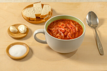 Vegetable soup in a soup bowl with bread, salt and garlic on a wooden background. Cabbage soup. Borsch