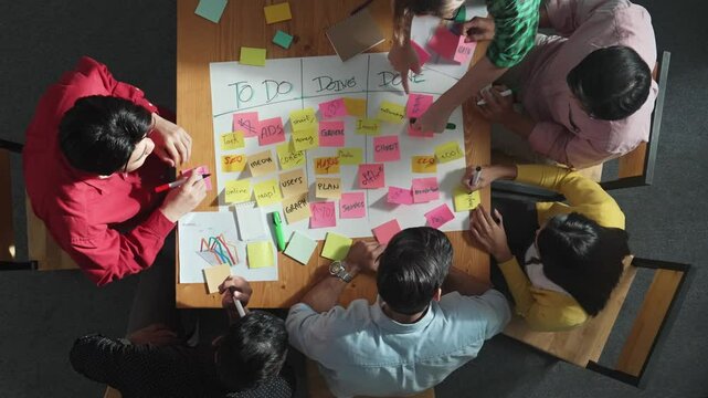 Top view of people writing and making scrum task board while writing marketing and planning strategy at colorful sticky notes. Smart team manage work performance by using kanaban board. Convocation.