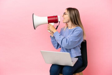 Young woman sitting on a chair with laptop over isolated pink background shouting through a megaphone