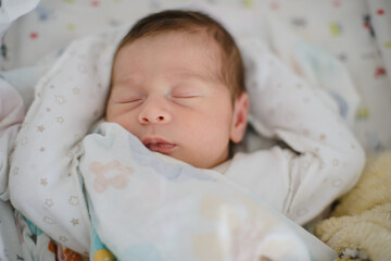 Portrait of a newborn baby in a bodysuit sleeping in his arms. Just born