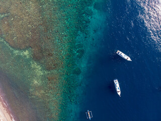 Aerial view of boats floating near a vibrant coral reef. © Marcel