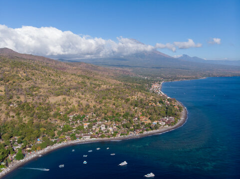 Scenic coastal view with boats along the shoreline and mountains in the background.
