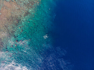 Aerial view of a boat floating on crystal-clear blue waters near a coral reef.