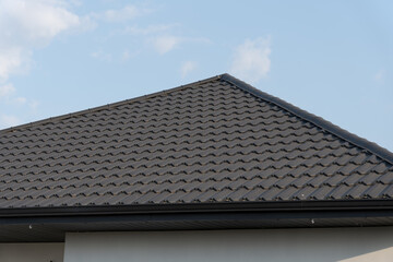 Newly installed metallic roofing boasts an elegant tile pattern, reflecting sunlight against a backdrop of a clear blue sky, showcasing craftsmanship and durability