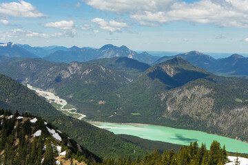 A breathtaking view of a serene turquoise lake surrounded by lush mountains under a partly cloudy sky.