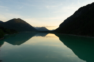 Fototapeta premium Serene landscape with a lake reflecting mountains at sunset.