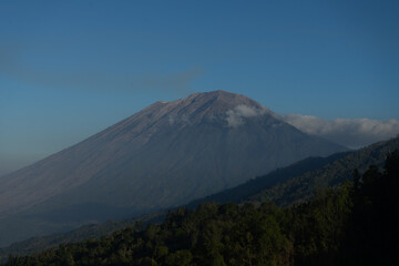 A majestic mountain surrounded by lush greenery under a clear blue sky.