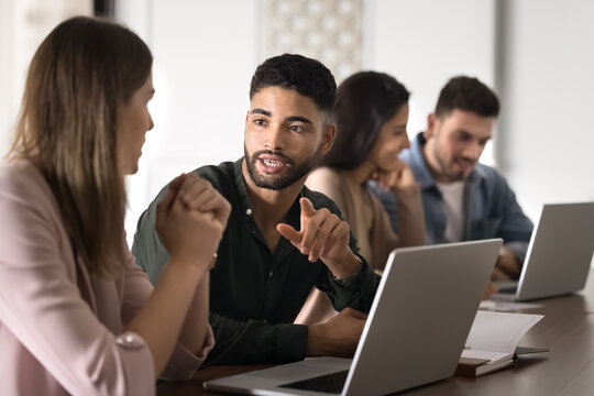 Handsome young Middle Eastern company intern talking to coworker woman at laptop, discussing corporate professional education, training task. Two colleagues, partners working at computer together - Powered by Adobe