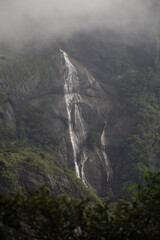 A misty waterfall cascades down a rocky cliff surrounded by lush greenery.
