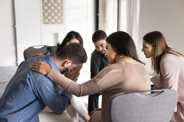 Diverse young people with psychological problems meeting for group therapy, emotional support session, sitting in circle, giving comfort, sympathy to crying depressed desperate man