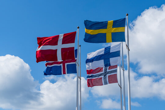 Scandinavian countries flags waving on metal poles against blue sky.