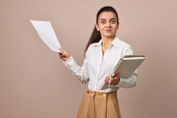 surprised businesswoman in white shirt holding folders with documents on beige background