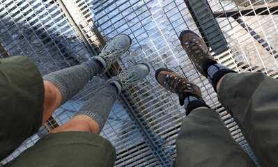 hikers legs with hiking boots above a metal grid suspended high over a glacier in the high mountains