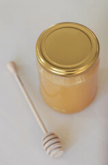 A minimalist still life photograph showcasing a glass jar filled with golden honey and a wooden honey dipper. The light background enhances the warm tones of the honey. Stock photo