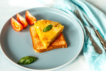 Spanish omelette or tortilla de patata with potatoes and onions on toast with tomatoes and basil on a blue plate. Typical Spanish cuisine.