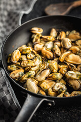 Shelled mussels meat in pan on black table.