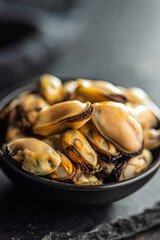 Shelled mussels meat in bowl on black table.