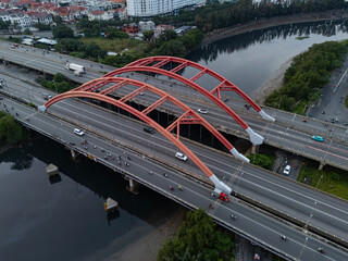 Traffic bridge over river in Ho Chi Minh City, Vietnam from aerial view featuring two large red steel arches and a wide, ten lane highway for heavy vehicles. High angle with reflection