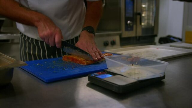 Professional chef cuts up and weighs fish as he prepares food in a professional kitchen