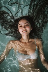 Obraz premium A carefree Asian girl enjoys floating in a pool, basking in the warmth of natural light.