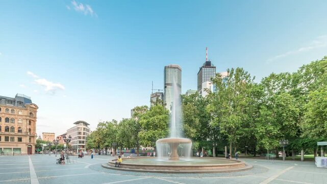 Opera Square (Opernplatz) timelapse hyperlapse in downtown Frankfurt, Germany, showcases a fountain with skyscrapers and towers in the background, surrounded by trees and city life under evening sky