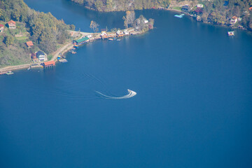Aerial view of a speedboat making waves on a serene lake surrounded by lush greenery, perfect for a...