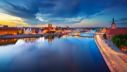 Obraz premium flyingover oder river to grunwaldzki bridge in wroc aw passing bye rushing traffic on the bridge illuminated historic buildings and bridges beautiful sky light reflections on blurred water