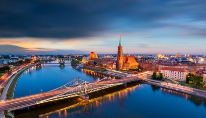 Fototapeta premium flyingover oder river to grunwaldzki bridge in wroc aw passing bye rushing traffic on the bridge illuminated historic buildings and bridges beautiful sky light reflections on blurred water