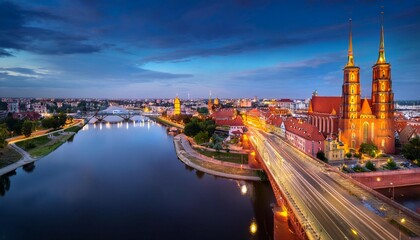 Naklejka premium flyingover oder river to grunwaldzki bridge in wroc aw passing bye rushing traffic on the bridge illuminated historic buildings and bridges beautiful sky light reflections on blurred water