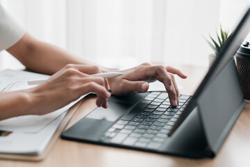 Close-up of hands typing on a laptop and using a stylus on a tablet in a modern office environment.