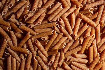 Uncooked Whole Grain Penne Rigate Pasta: A Culinary Canvas of Whole Wheat Macaroni, Creating a Lively and Textured Background for Gourmet Cooking. Whole Grain Dry Pasta. Whole Wheat Raw Macaroni