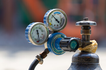 A blue and white pressure gauge sits on top of an oxygen cylinder tank.
