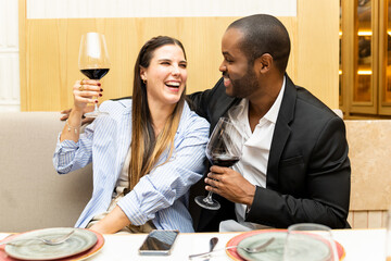 A couple of different ethnicities in their 30s are drinking and eating at a trendy restaurant. The...