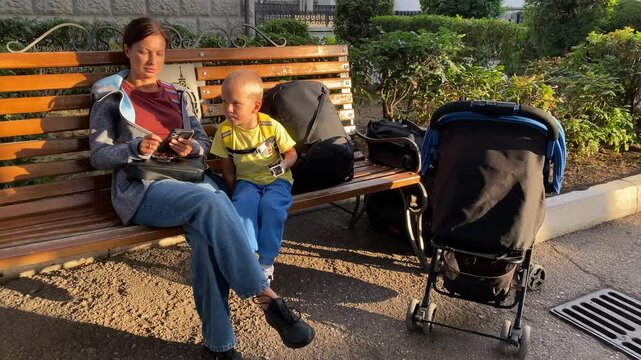Family traveling with cat in soft carrier. Woman with small child with luggage, big grey adult cat in pet carrier in baby carriage at railway station waiting for train to arrive.