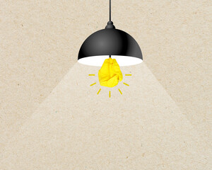 Yellow paper light bulb inside of a hanging lamp or drop light infront of recycled brown paper metaphor for new idea and inspiration