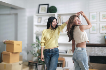 Two cute asian women are happily dancing in their home because they are delighted with their successful online business.