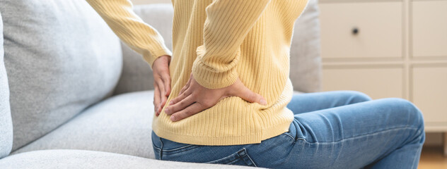 Close-up woman massaging her lower back has back pain because of sitting posture during work in...