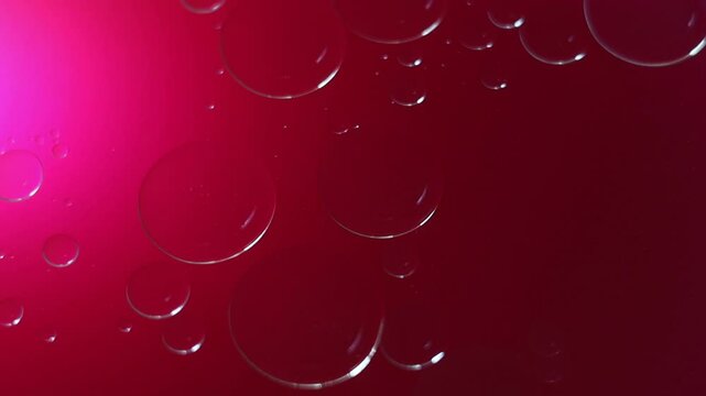 Una toma de cerca de varias burbujas de agua y aceite en movimiento en un fondo de color rosado